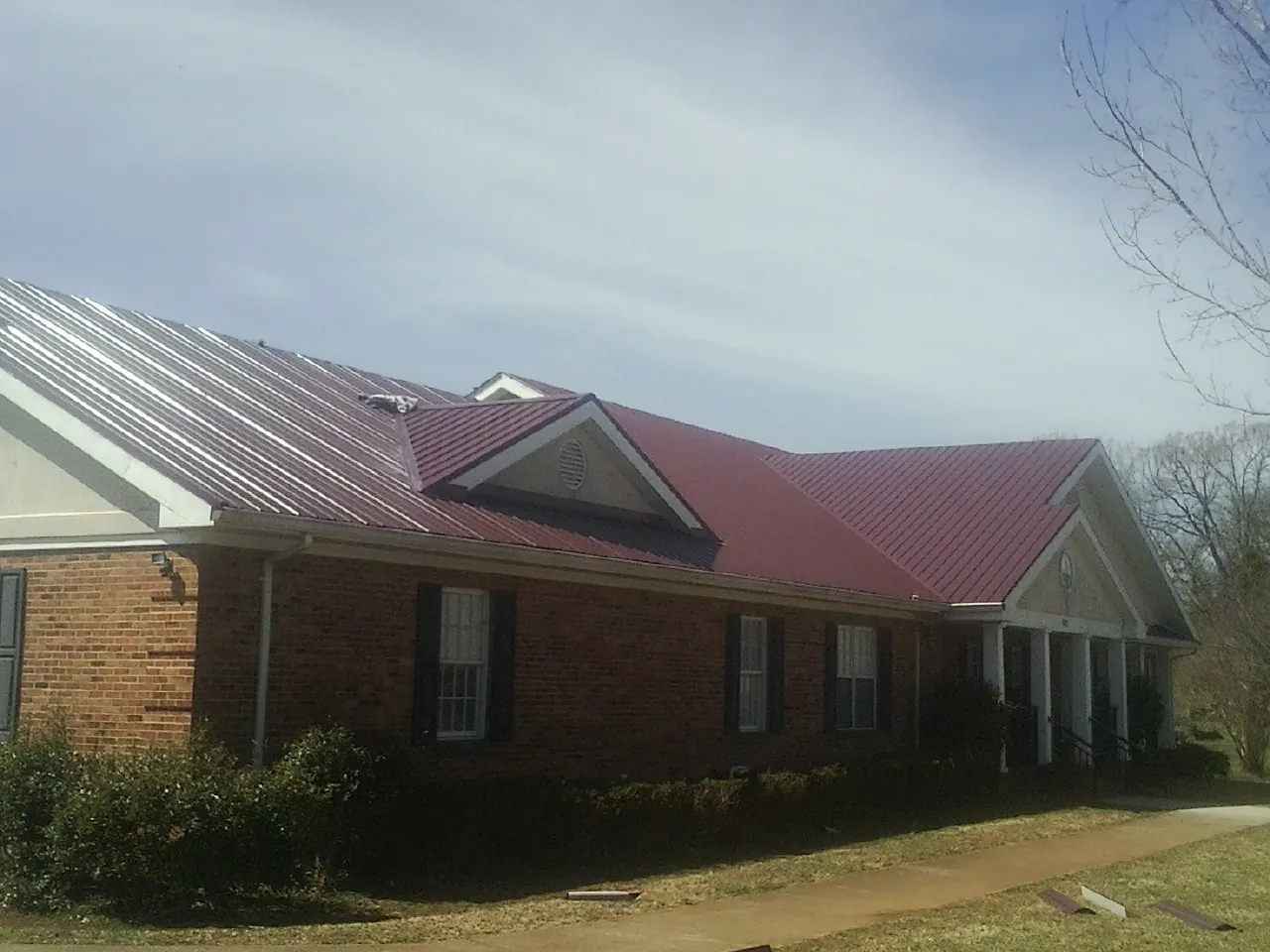 Red metal roof with gabled entries on a long brick building, from a Hail Damage Roof Repair job in Ithaca